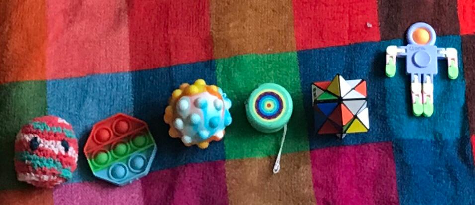 A selsction of figets toys: crochet ball, poppet, poppet ball, a yoyo, a rubix toy, and bendy fidget person